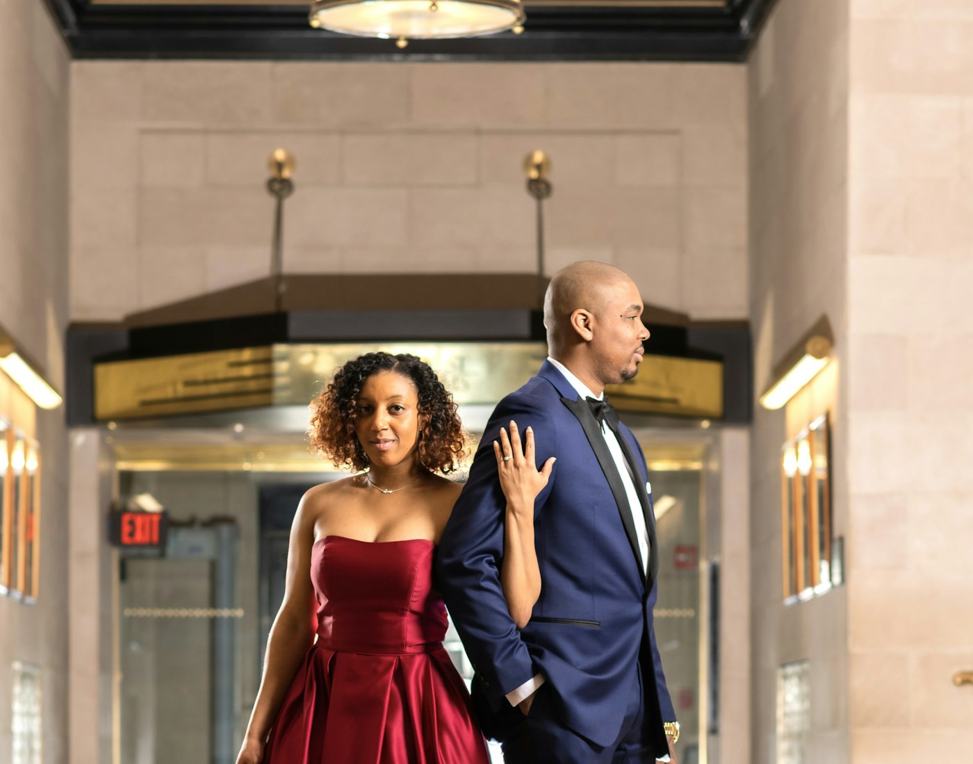 Couple élégant : femme en robe de soirée rouge et homme en costume bleu nuit.